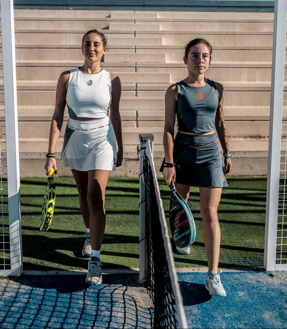 Two women on a Padel court holding rackets, wearing Drybreak clothes.